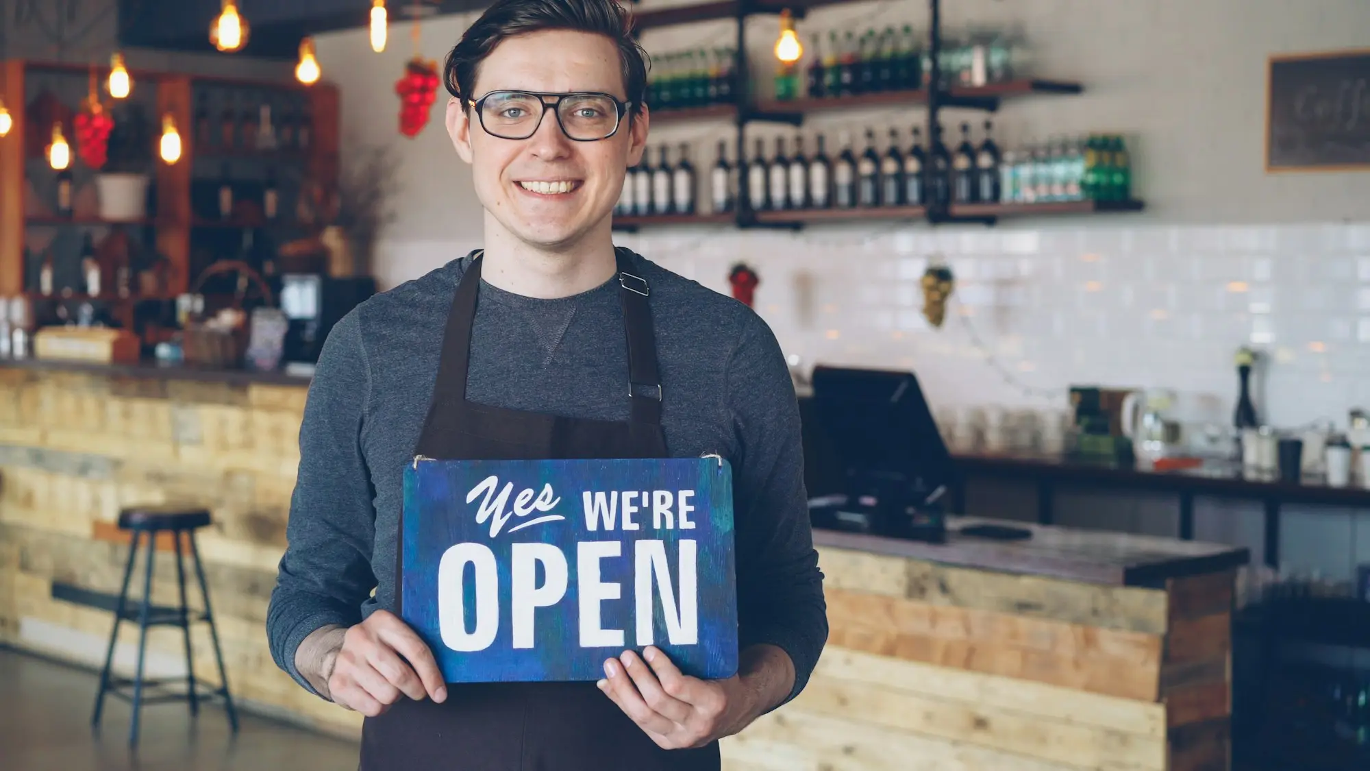 Café owner smiling and holding an open sign in their shop